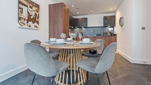 Een moderne eetruimte met een ronde tafel, gestoffeerde grijze stoelen en een houten stoelrand.