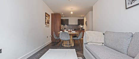 A modern living room with a grey sofa, a white coffee table, and a dining area with a wooden table and chairs.