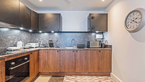 Een moderne keuken met houten kastjes, een inbouwoven, een magnetron en een klok aan de muur.