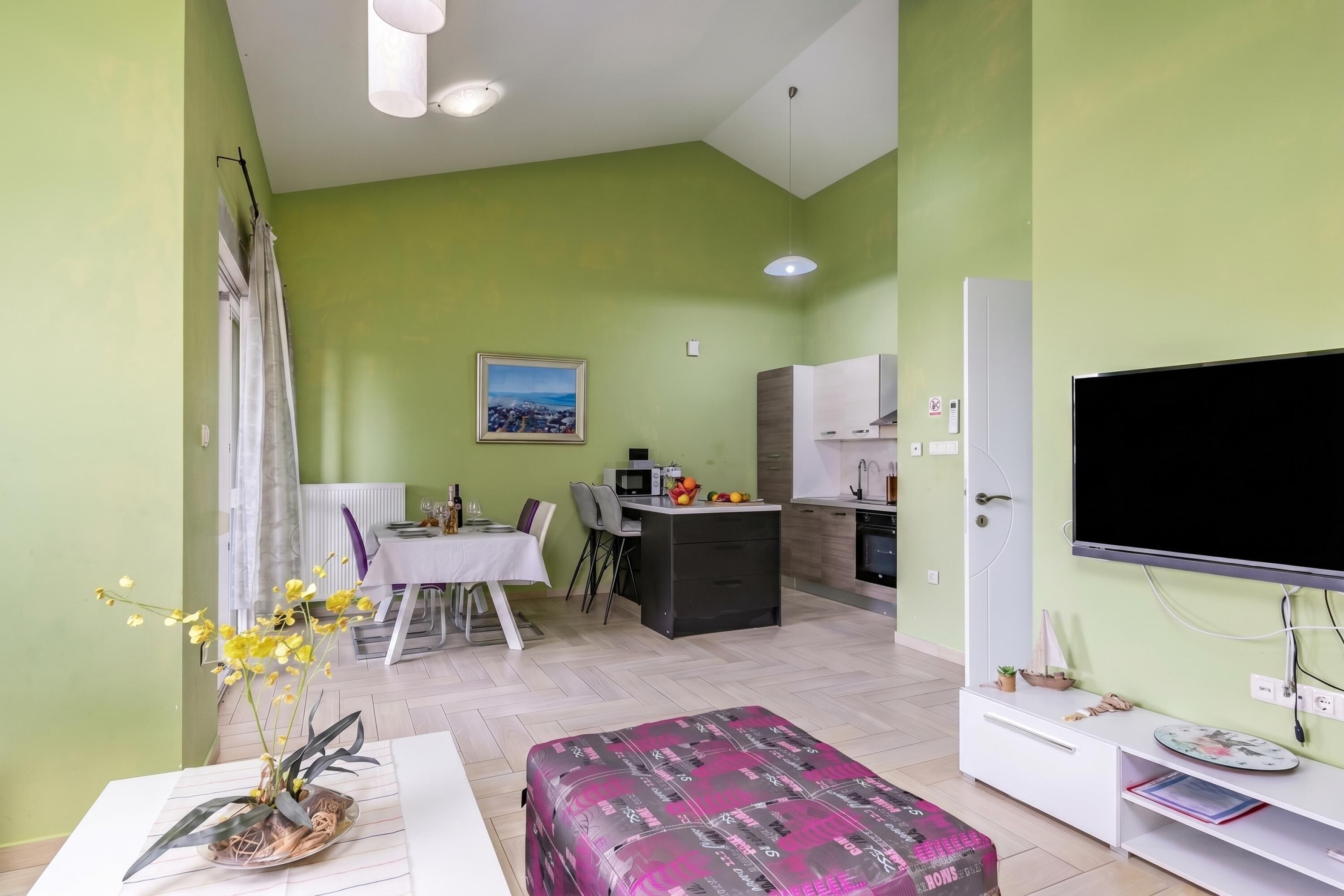 Uma sala de estar com área de jantar, cozinha compacta e televisão.