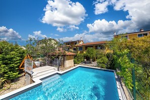 Ein Schwimmbecken mit Holzterrasse, umgeben von Grünflächen und einem eingezäunten Bereich.