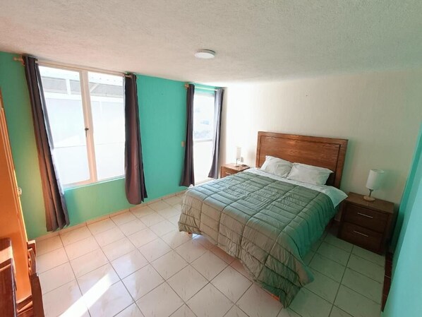 Un dormitorio con cama, mesita de noche, lámpara y ventana con cortinas.