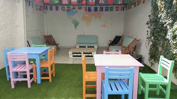 A patio area with colorful chairs and tables, a world map mural, and flags on the wall.