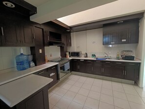 Una cocina con armarios oscuros, un dispensador de agua grande, una estufa y un microondas.