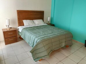 Une chambre Ă coucher avec une tĂȘte de lit en bois, une couvre-lit verte, deux tables de chevet avec des lampes et un plancher carrelĂ©.