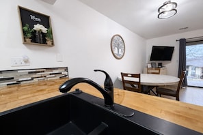 A modern kitchen with a black sink, wooden countertop, and a dining area with a round table and chairs. - Clubhouse Cove at Pointe Royale (Branson)