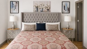 Una camera da letto con testiera imbottita, copriletto decorato, due comodini con lampade e opere d'arte appese alle pareti.