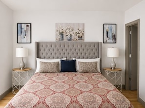 A bedroom with a tufted headboard, a patterned bedspread, two bedside tables with lamps, and framed artwork on the walls. - Clubhouse Cove at Pointe Royale (Branson)