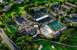 An aerial view of a residential area with houses, a swimming pool, tennis courts, and a golf course. - Clubhouse Cove at Pointe Royale (Branson)