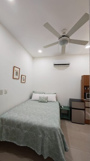 Ein Schlafzimmer mit Bett, Deckenventilator, Klimaanlage, kleinem Tisch und Mikrowelle.