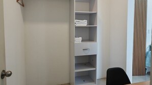 Huoneessa on puinen pöytä, valkoinen hyllyillä varustettu vaatekaappi ja ovi, jossa on kahva.