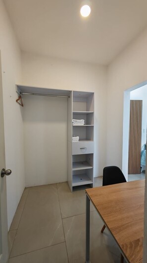 Ein Zimmer mit einem Holztisch, einem weißen Kleiderschrank mit Regalen und einer Tür mit Griff.