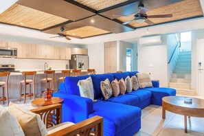 Ein modernes Wohnzimmer mit einem blauen Sofa, Holzstühlen, einem Couchtisch und einem Deckenventilator.