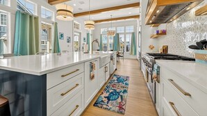 Cocina moderna con una isla grande, vigas de madera, iluminación colgante y vistas al área de comedor.