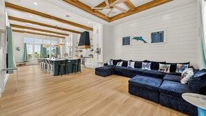 Amplia sala de estar con un sofá seccional azul oscuro, vigas de madera en el techo y una cocina al fondo.