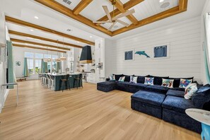 Ein geräumiger Wohnbereich mit einem dunkelblauen Ecksofa, Holzbalken an der Decke und einer Küche im Hintergrund.