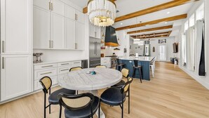 Una cocina moderna con armarios blancos, una mesa redonda para comer y una lámpara de araña.