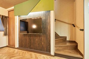 Ein Korridor mit Holzboden, einer Treppe mit Handlauf und einem an der Wand montierten Fernseher.