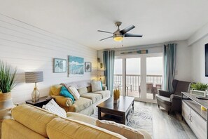 A living room with a sofa, a coffee table, a TV, and a ceiling fan. - Oceanfront condo with spacious private balcony, pool & direct beach access (North Myrtle Beach)