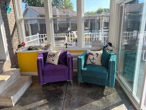 Habitación soleada con dos sillas, una mesita y una ventana que da a un patio cercado.