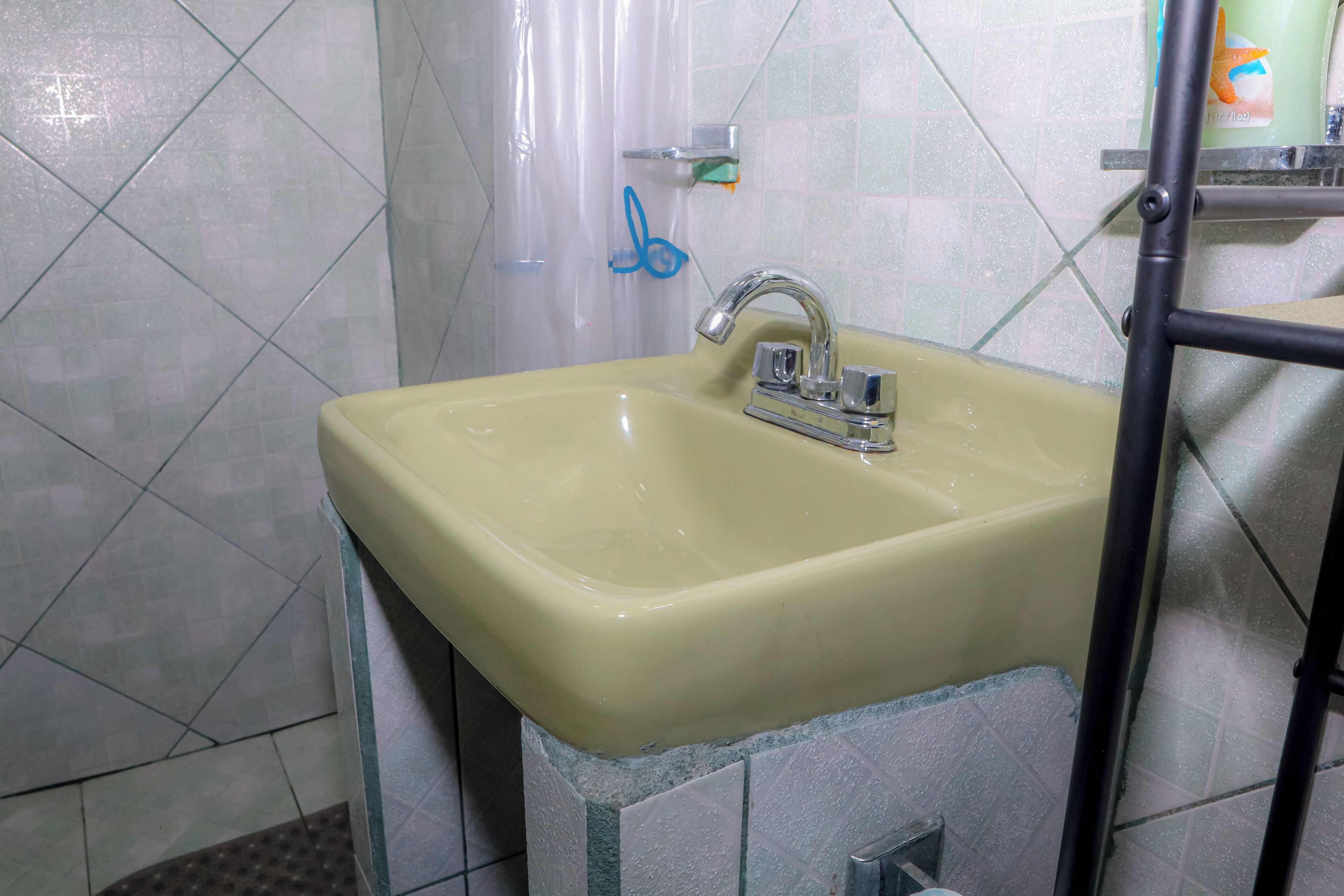 A bathroom with a sink, a shower curtain, and a soap dispenser.
