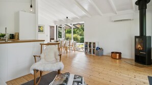A spacious room with a wooden floor, a white chair, a dining table with chairs, a bookshelf, and a wood-burning stove. - Lovely home in Vejby with WiFi (Vejby)