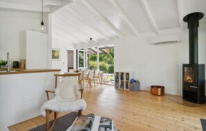 A spacious room with a wooden floor, a white chair, a dining table with chairs, a bookshelf, and a wood-burning stove. - Lovely home in Vejby with WiFi (Vejby)