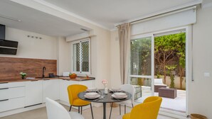 Une cuisine moderne avec des meubles blancs, un plan de travail en bois et un coin repas agrémenté de chaises jaunes et d’une table ronde.