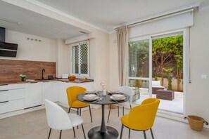 A modern kitchen with white cabinets, a wooden countertop, and a dining area with yellow chairs and a round table. - Brisa de Banús by Lica Homes (Marbella)