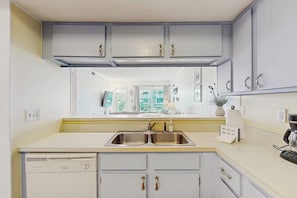 A kitchen with a double sink, a dishwasher, and a coffee maker. - Oceanview condo with pool, private balcony & direct beach access (Murrells Inlet)