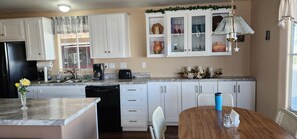 A kitchen with white cabinets, a dishwasher, a coffee maker, and a dining table with chairs. - Charming 2-bedroom 2 bath house with AC in a gated 55 and over community in Mesa (Mesa)