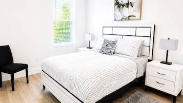 Un dormitorio con cama, mesitas de noche, una silla, un ventanal con persianas y aire acondicionado instalado en la pared.