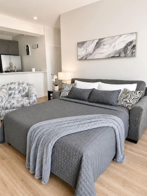Ein Schlafzimmer mit einem großen Bett, einem grauen Sofa, einem kleinen Tisch und einem an der Wand hängenden Kunstwerk.