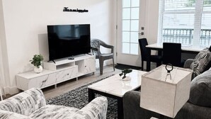 A modern living room with a flat-screen TV, a sofa, a coffee table, and a dining area with a chair and table. - Stylish 1 BR Suite • Downtown • Convention Center (Hot Springs)