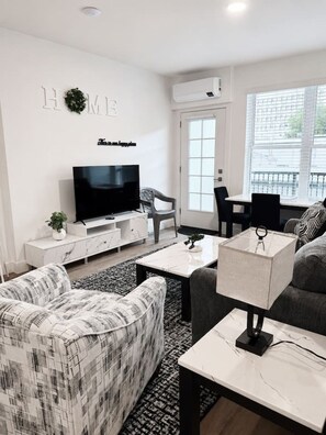 Ein modernes Wohnzimmer mit Flachbildfernseher, einer Couch, einem Couchtisch und einem Essbereich mit Stuhl und Tisch.