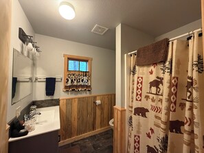 A bathroom with a wooden vanity, a window with a curtain, a mirror, and a shower curtain with animal prints.