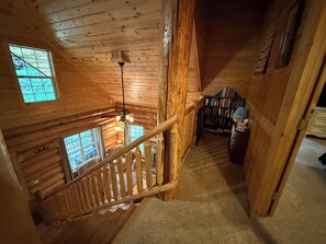 A wooden interior with a staircase, bookshelves, and a view through a window.