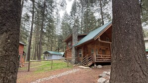 Una cabaña rústica de troncos con chimenea de piedra, rodeada por un bosque.