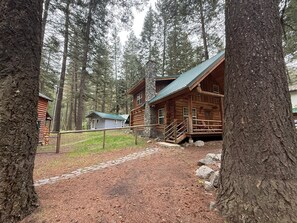 A rustic log cabin with a stone chimney, surrounded by a forest.