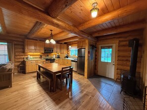 A wooden cabin interior with a kitchen, dining area, and a fireplace.
