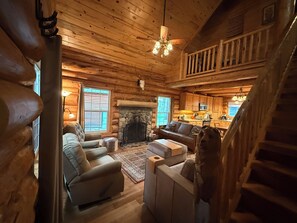 Interior de una cabaña de troncos con chimenea, muebles de madera y zona de cocina.