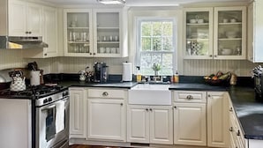 Une cuisine avec des meubles blancs, une cuisinière et une fenêtre.