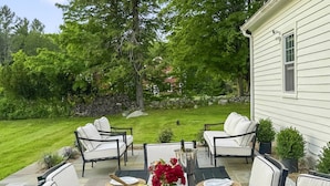 Une terrasse extérieure avec une table à manger pour quatre personnes, entourée de chaises blanches dotées de coussins.