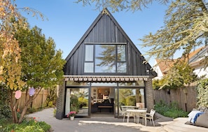 A modern house with a triangular roof, large windows, and a patio with outdoor furniture.