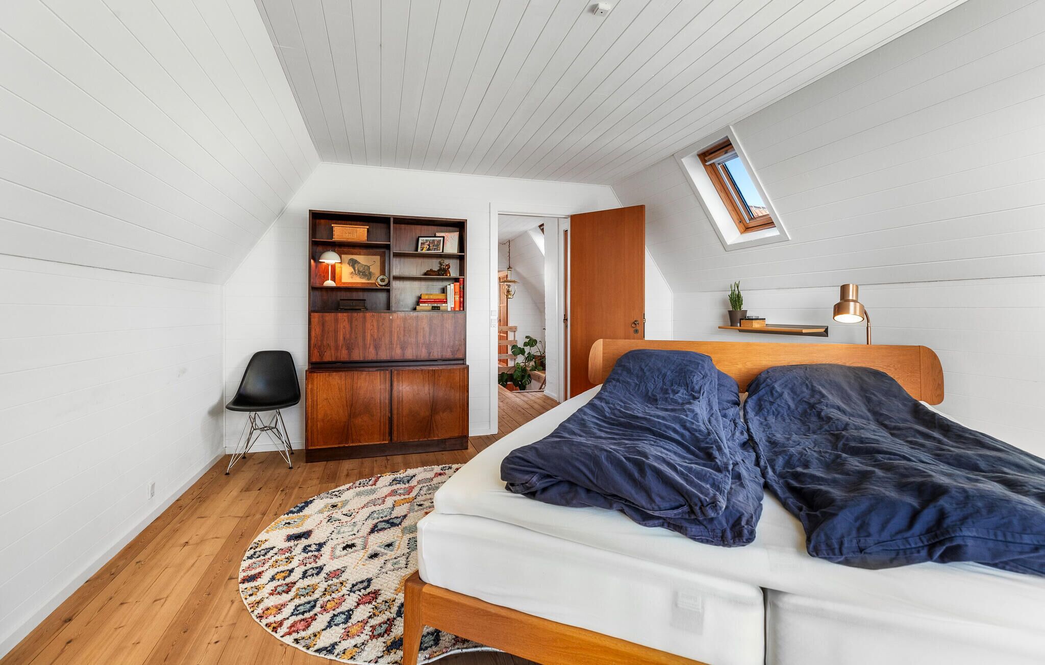 Een slaapkamer met een bed, een bureau, een stoel, een kledingkast en een dakraam.