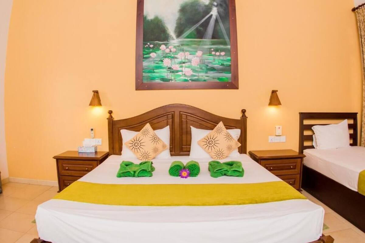 A hotel room with a bed, two nightstands, a painting of a lotus pond, and a yellow bedspread.