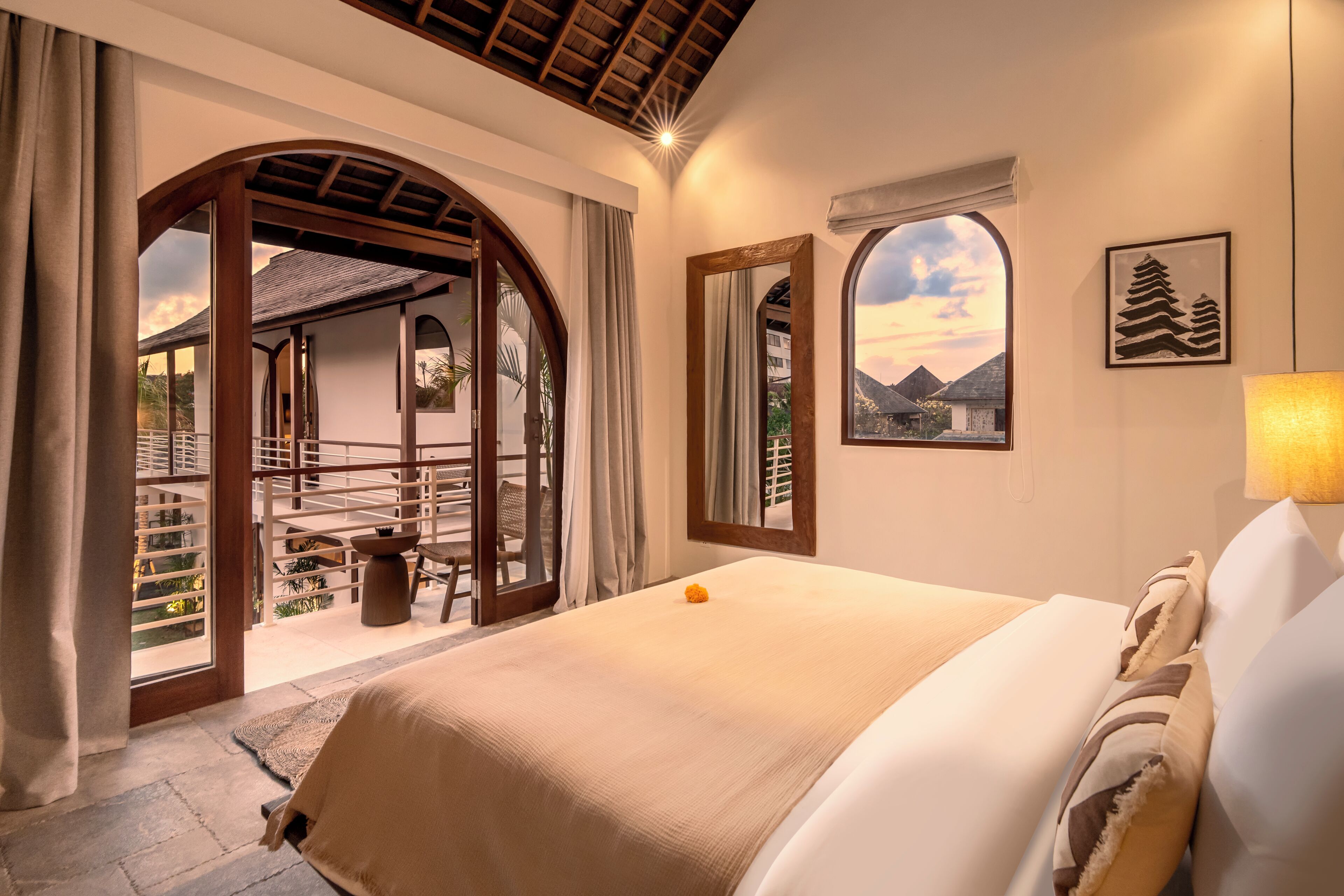 A hotel room with a bed, a view of the outside, a window with a view of mountains, and a framed picture on the wall.