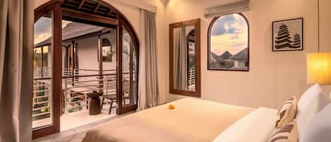 A hotel room with a bed, a view of the outside, a window with a view of mountains, and a framed picture on the wall.