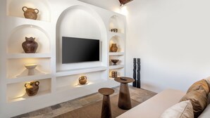 Een moderne woonkamer met een flatscreen televisie aan een witte muur, omringd door planken met diverse decoratieve objecten.