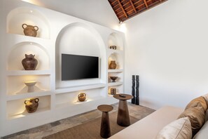 A modern living room with a flat-screen TV mounted on a white wall, surrounded by shelves with various decorative items. - Villa Amara by Alfred in Bali (Seminyak)